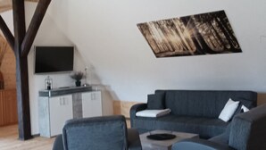 Un espacio habitable moderno con techo inclinado, un televisor de pantalla plana en la pared, un sofá de color oscuro y una pequeña mesa de centro.