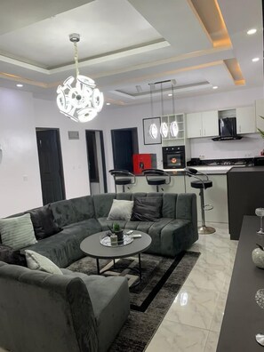Relax in this stylish living room with a large sofa, glass coffee table, and modern kitchen area.