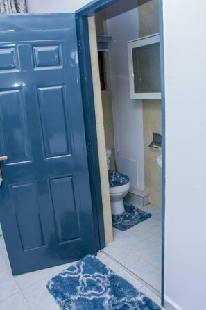 A bathroom with a toilet, mirror, and shelf.