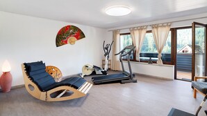 Una habitación con una mecedora de madera, una cinta de correr y un ventilador en el alféizar de la ventana.