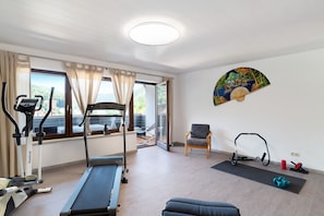 A gym with exercise equipment, a chair, a mat, and a painting on the wall.