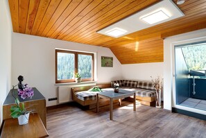A cozy room with a sloped ceiling, wooden flooring, a bench, a table, and a window with a view of trees.