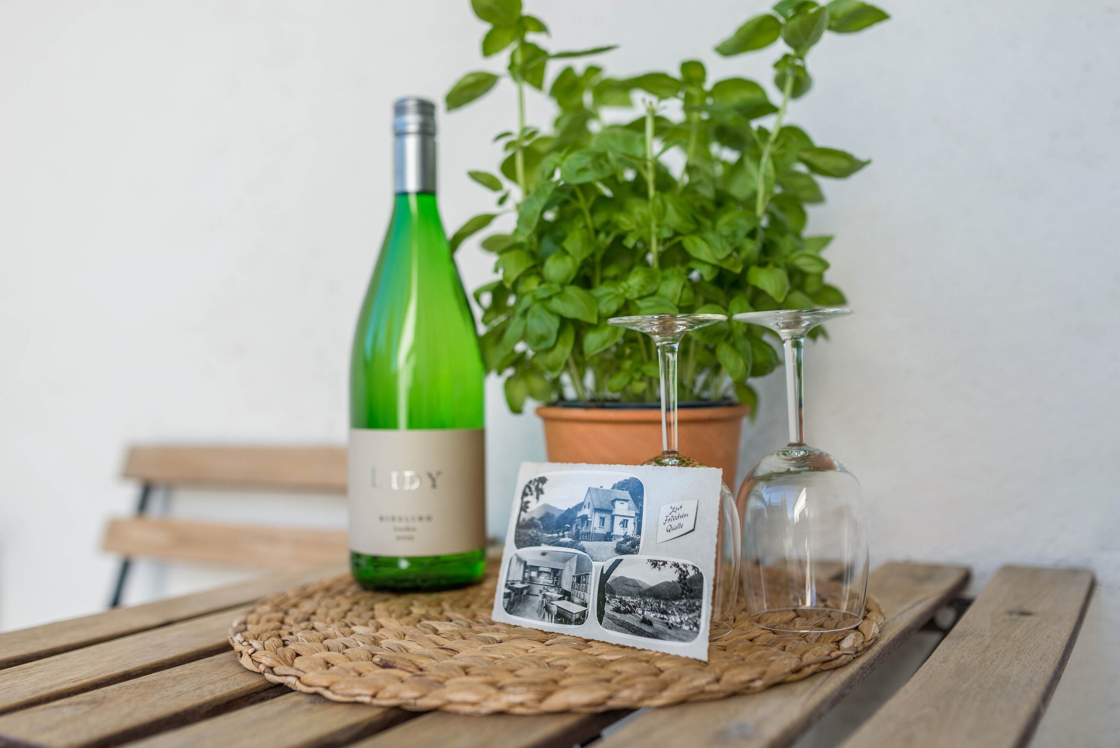 A bottle of wine, a glass, and a potted plant on a wooden table.