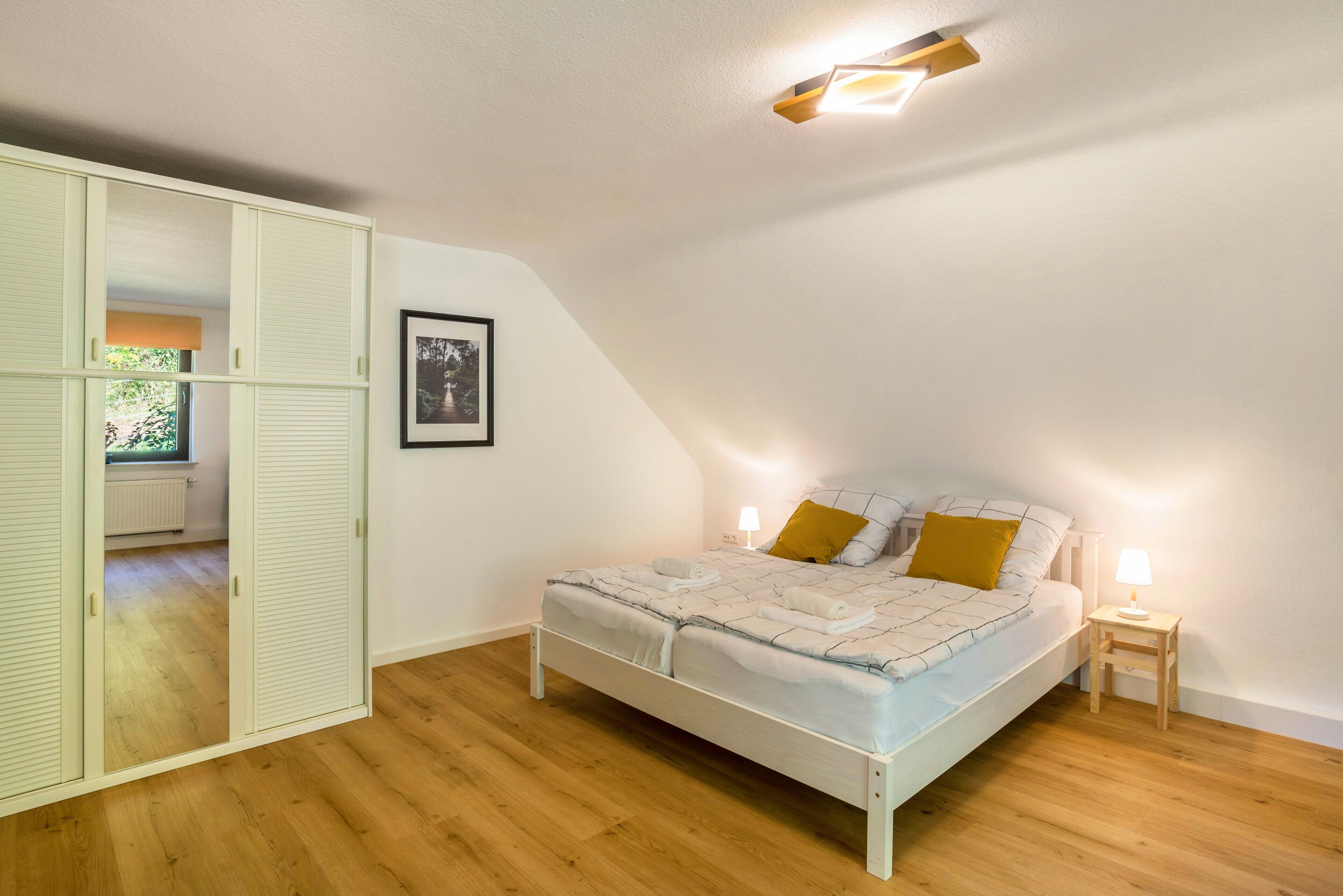 Ein Schlafzimmer mit einem Bett, Nachttischlampen, einem gerahmten Bild an der Wand und einem Fenster mit Jalousien.