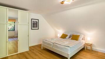 Ein Schlafzimmer mit einem Bett, Nachttischlampen, einem gerahmten Bild an der Wand und einem Fenster mit Jalousien.