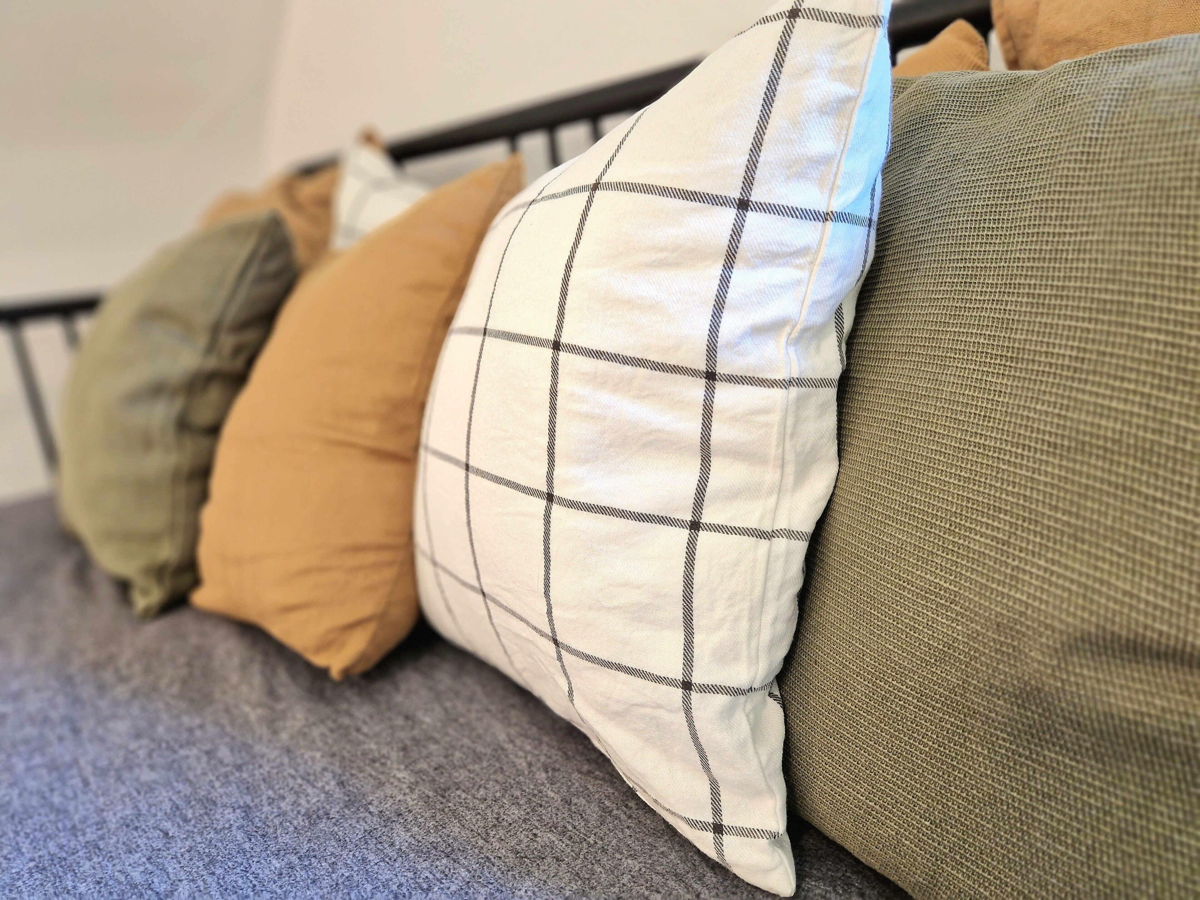 Een bed met een grijze deken en meerdere kussens in verschillende kleuren en patronen.