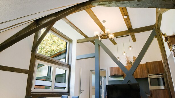 Eine rustikale Küche mit freiliegenden Holzbalken, einem großen Fenster mit Jalousien und einem modernen Herd.