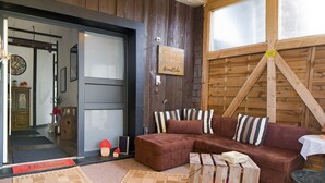 Ein gemütliches Wohnzimmer mit einem braunen Ecksofa, gestreiften Kissen, einer Holzwand und einer Tür mit Milchglasfenstern.
