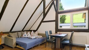 A room with a bed, a table, and chairs, a window with a view of a green landscape, and exposed wooden beams on the ceiling. - Apartment 'Ferienwohnung 2' with Shared Garden and Wi-Fi (Vöhrenbach)