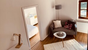 A living room with a sofa, a small side table, a lamp, a radiator, and a window. - Apartment 'Felix Living 7' with Private Terrace and Wi-Fi (Passau)