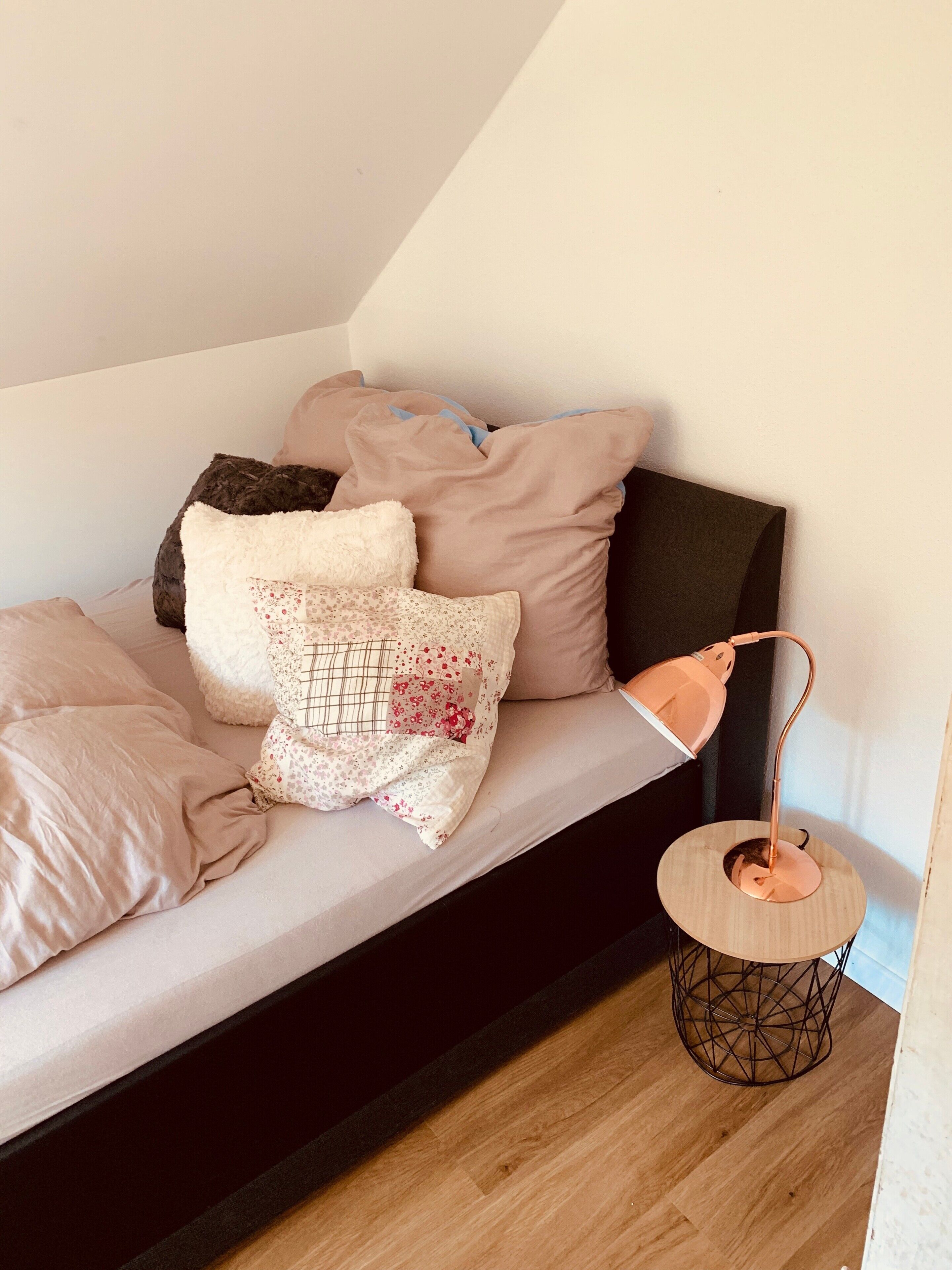 Een bed met meerdere kussens, een bedlamp en een klein rond tafeltje.