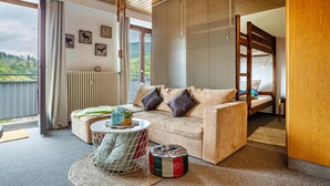 Ein gemütliches Zimmer mit einer Couch, einem kleinen runden Tisch, einer Hängeleuchte und Blick ins Freie.