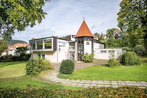 A building with a glass facade, a red-tiled roof, and a small tower-like structure. - Holiday Apartment "Grundblick" with Mountain View, Balcony & Wi-Fi (Bad Grund)