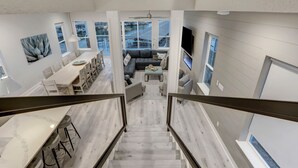 Amplia sala de estar con escalera que conduce a un balcón, comedor y zona de estar con televisor.