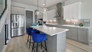 Una cocina moderna con una isla central, electrodomésticos de acero inoxidable y taburetes de bar azules.