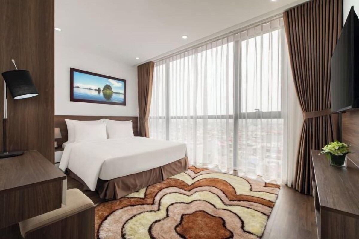 Une chambre d’hôtel avec un lit, un bureau, une chaise, une télévision et une fenêtre avec des rideaux.