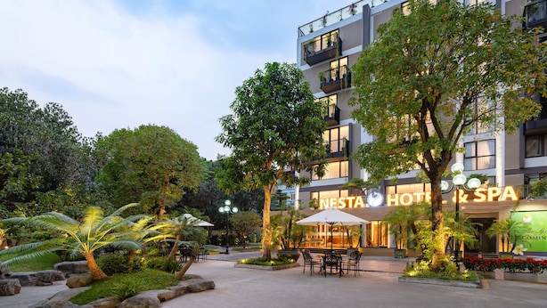 A modern hotel with a well-lit entrance, outdoor seating area, and lush greenery. - Nesta Hotel & Spa (Hanoi)