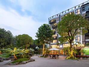 A modern hotel with a well-lit entrance, outdoor seating area, and lush greenery.