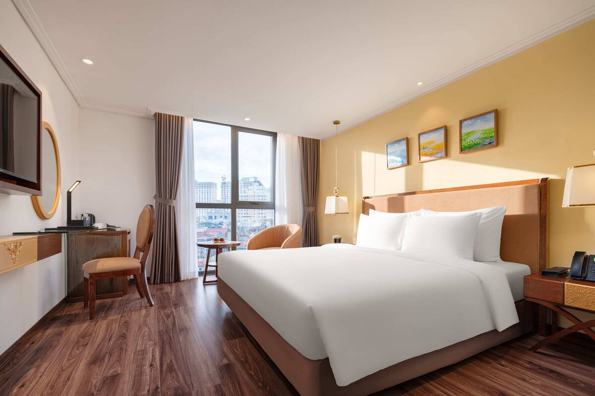 Een hotelkamer met een groot bed, een bureau met stoel, een televisie en een raam met uitzicht op de stad.