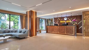 A modern hotel lobby with a reception desk, a sofa, and a large window offering a view of the outdoors. - Nesta Hotel & Spa (Hanoi)