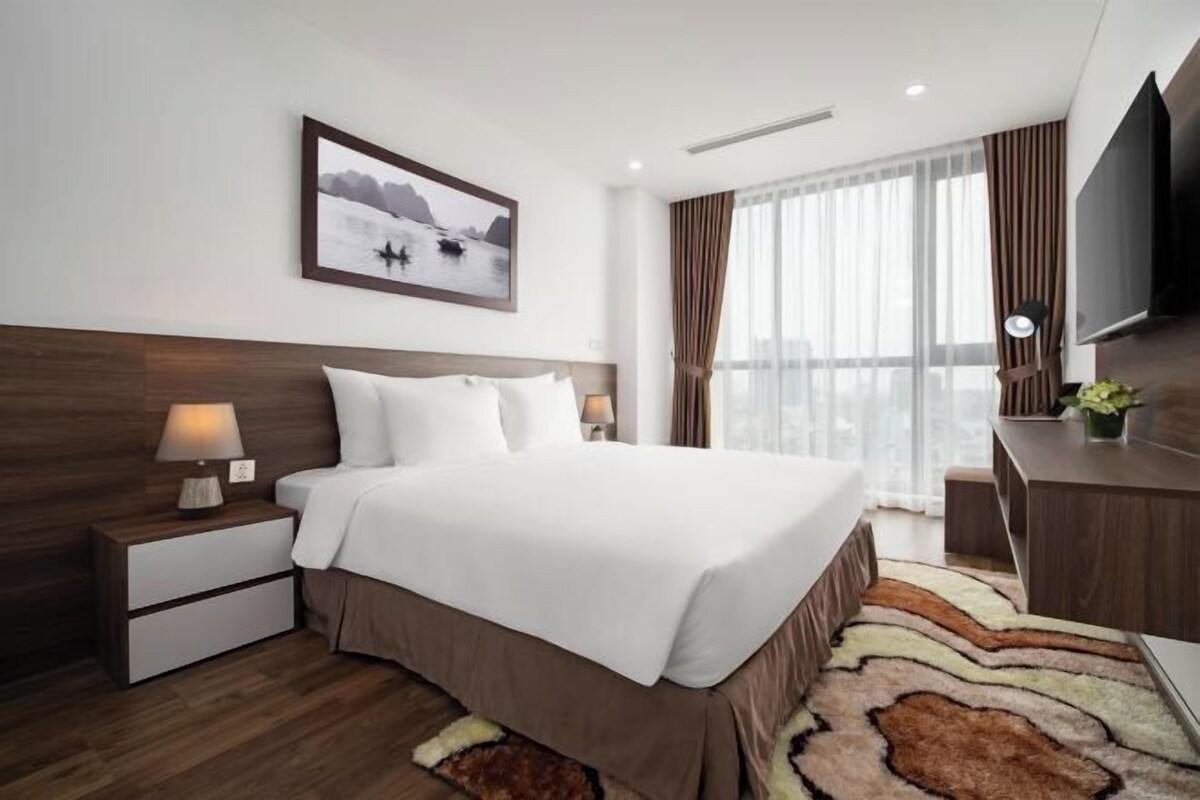 Une chambre d’hôtel moderne dotée d’un grand lit, d’une télévision à écran plat, d’un bureau et d’une fenêtre avec des rideaux.