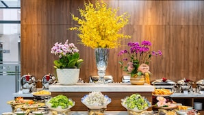 A buffet with various food items and decorative flowers. - Nesta Hotel & Spa (Hanoi)