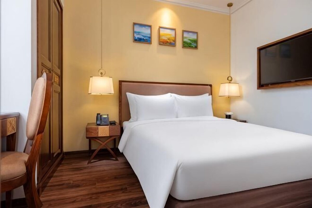 Une chambre d’hôtel avec un grand lit, deux lampes de chevet, une chaise, une table de chevet et un téléviseur fixé au mur.