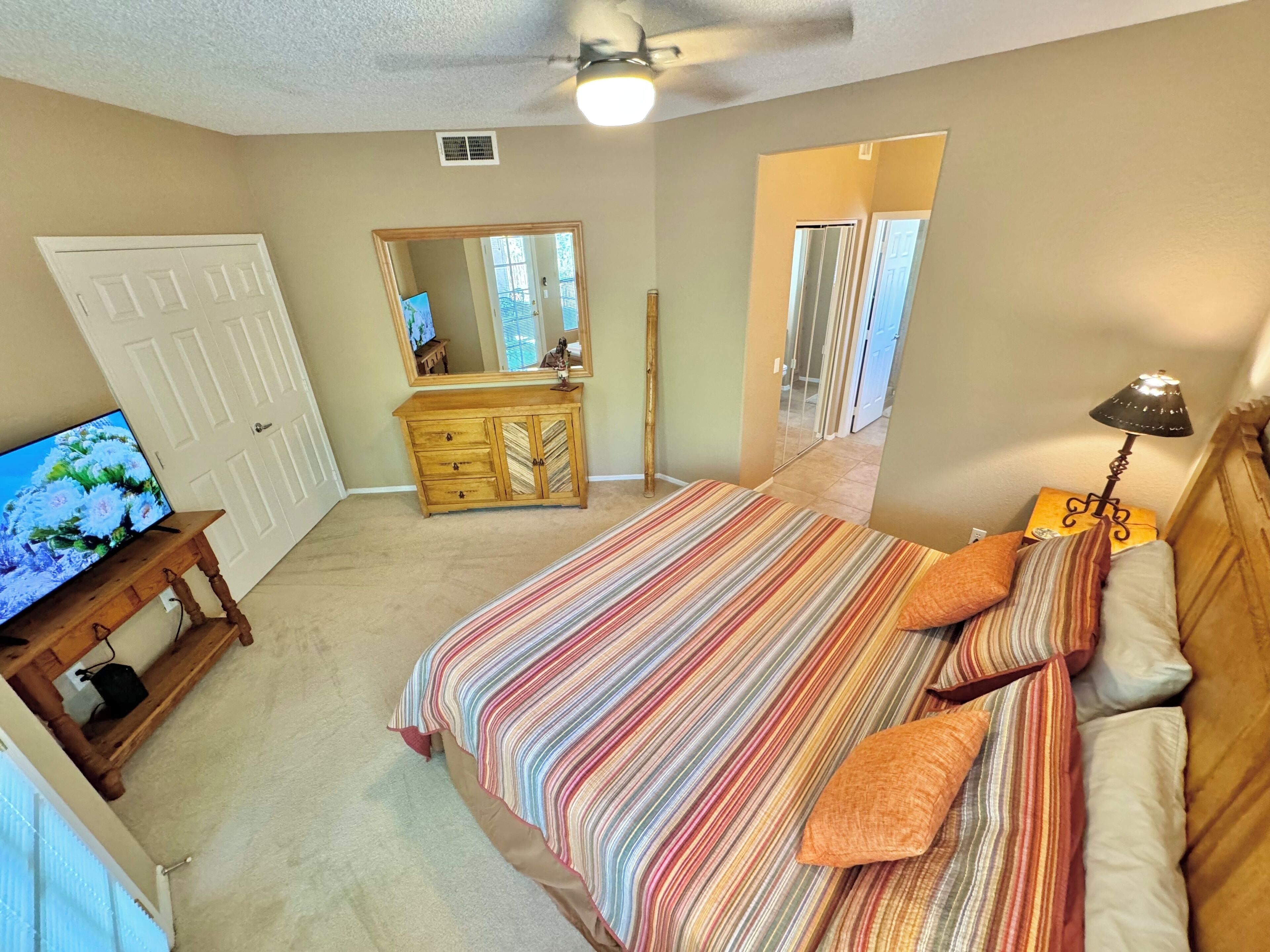 A bedroom with a bed, a dresser, a TV on a stand, a mirror, and a ceiling fan.