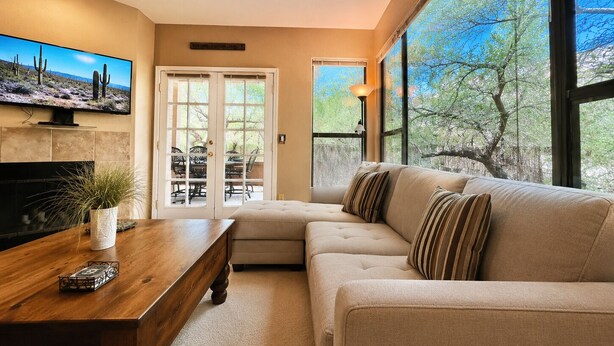 A living room with a sofa, a coffee table, a TV, and a ceiling fan. - Canyon Vista 🌵3br Retreat: Views, Hiking, Birds, Heated Pools, Spas, Court, Gym (Tucson)