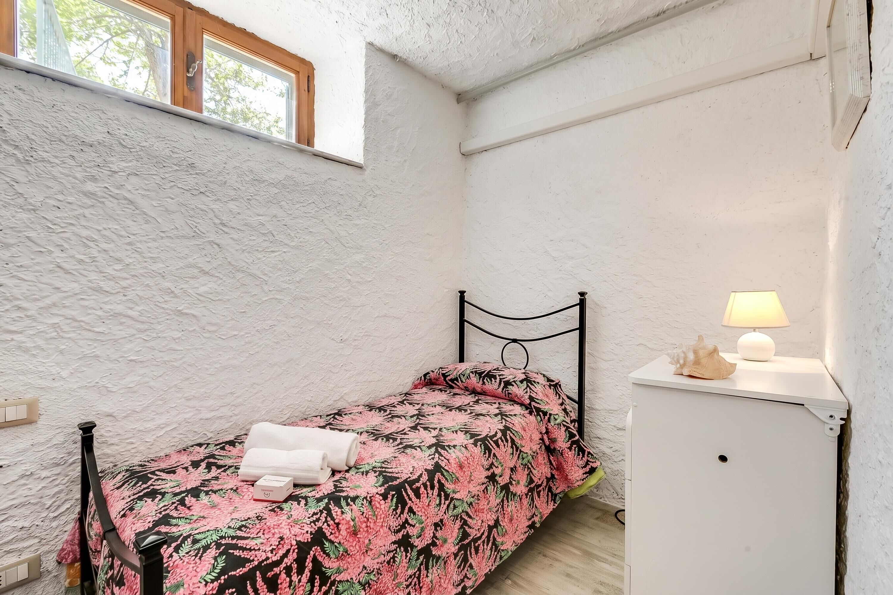 A small bedroom with a bed, a nightstand, a lamp, and a window.