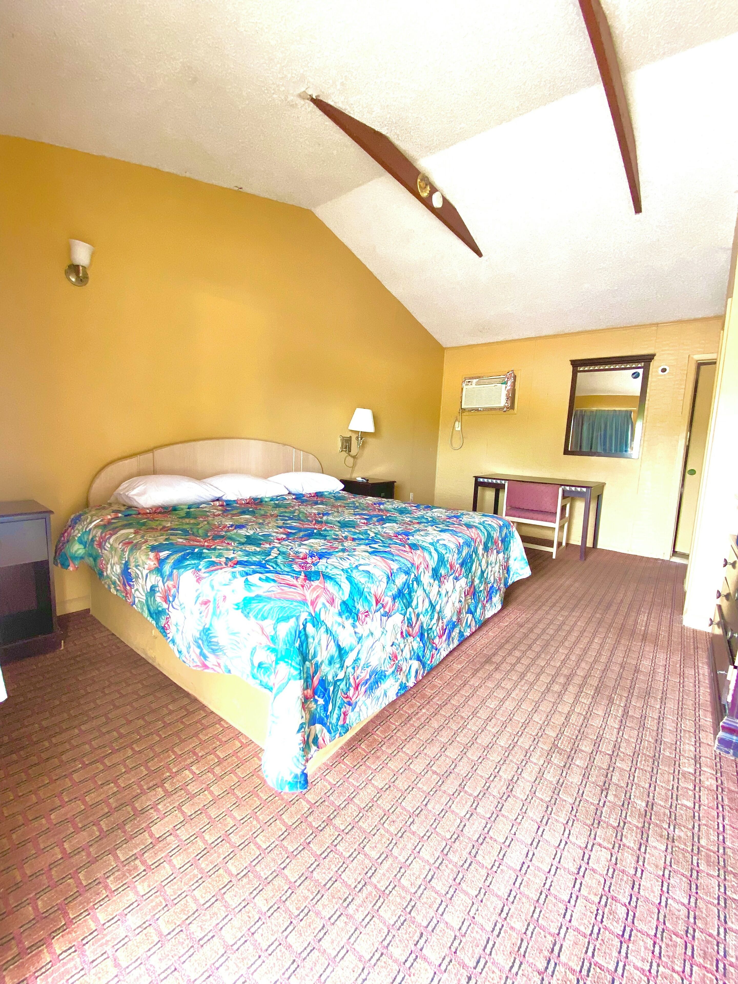 Quarto com cama, mesa de cabeceira, luminária, espelho e janela.