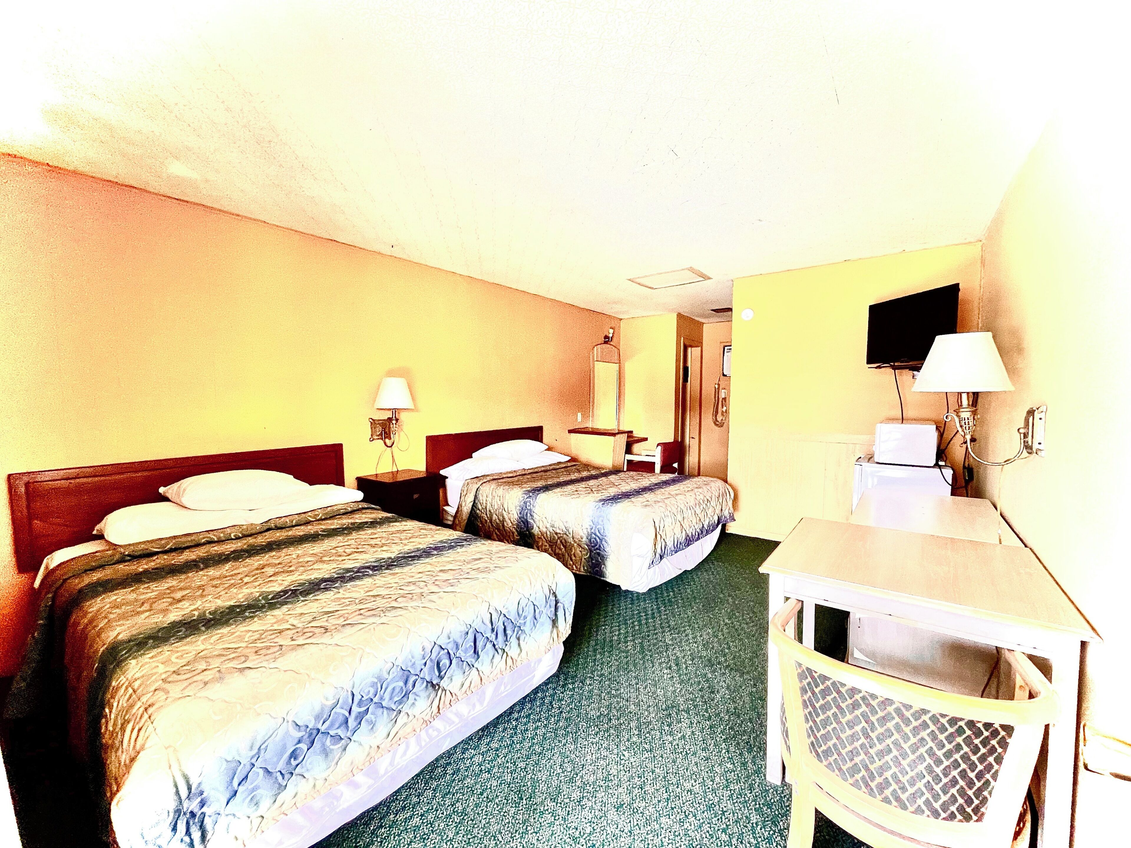 Habitación de hotel con dos camas individuales, un escritorio, una silla, un televisor y un espejo.