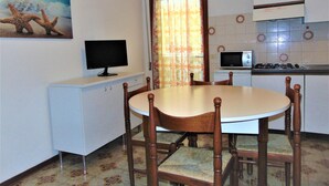 A compact kitchen with a dining table, chairs, a microwave, a stove, and a television.