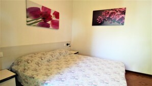 A bedroom with a floral bedspread, a nightstand, and two wall-mounted flower paintings.