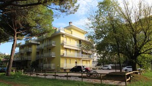 A multi-story yellow building with balconies, a paved parking area, and a grassy foreground.