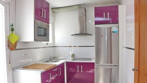 A compact kitchen with white and purple cabinets, a stainless steel refrigerator, a microwave, and a sink. - Apartment Malva in Conil (Conil de la Frontera)