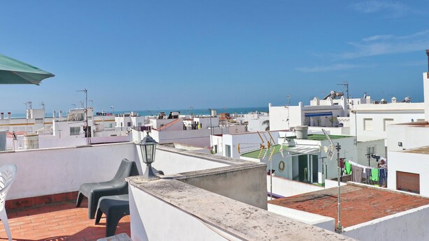 A rooftop terrace with a view of the sea, featuring a table and chairs, a lamp, and a clothesline with laundry. - Apartment Malva in Conil (Conil de la Frontera)