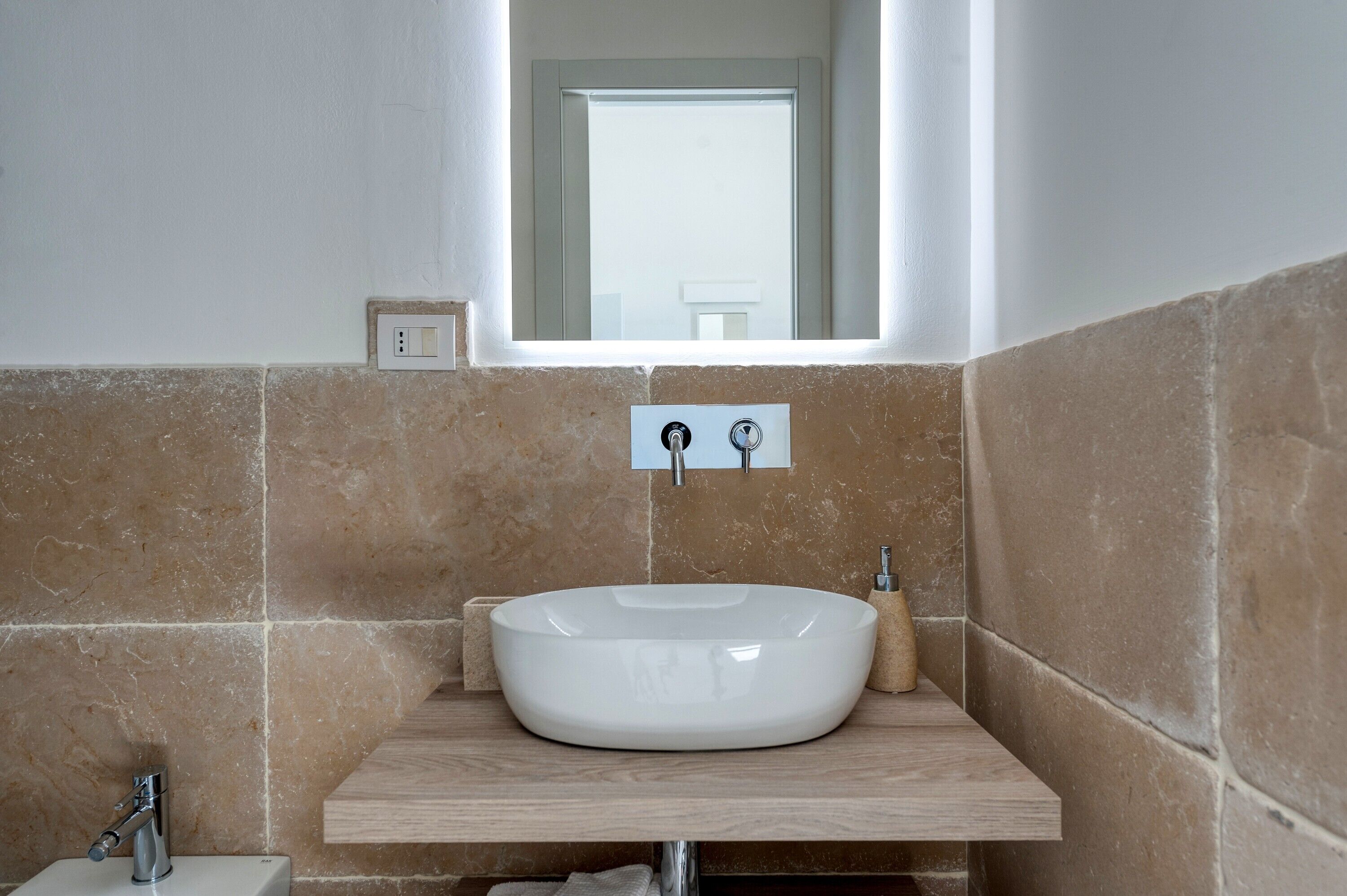 A bathroom with a white sink, beige tiles, a mirror, and a light switch.