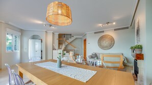 Un comedor amplio con una mesa de madera, sillas transparentes, una lámpara colgante y una escalera que sube a un nivel superior.