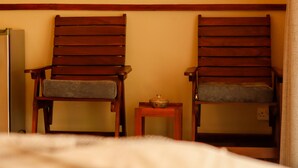 Una habitación con dos sillas de madera, una mesita con un cuenco y una cama con cubrecama blanco.