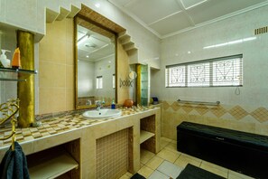A bathroom with a large mirror, a sink, a vanity, and a black storage unit. - Zambezi Family Lodge - Elephant Room (Victoria Falls)