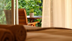 Una habitación con una silla de madera, una mesita con una planta en maceta, y vistas al exterior.