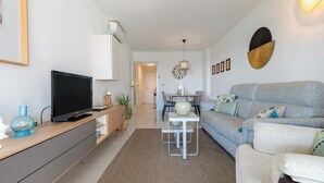 Uma sala de estar moderna com uma televisão de tela plana, um sofá cinza, uma mesinha branca e um tapete marrom.