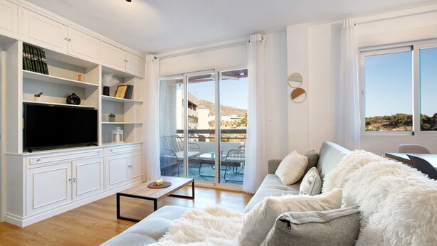 A modern living room with a sofa, TV, white cabinets, and a balcony with outdoor furniture. - Apartment 'Armonia' with Sea View, Wi-Fi and Air Conditioning (Torremolinos)