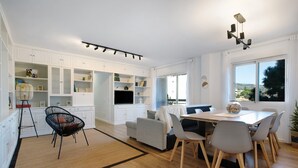 A modern kitchen with white cabinetry, a dining area with a wooden table and chairs, and a large window offering a view. - Apartment 'Armonia' with Sea View, Wi-Fi and Air Conditioning (Torremolinos)