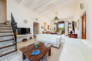 A spacious living area with a white sofa, a wooden coffee table, a TV, and a staircase.