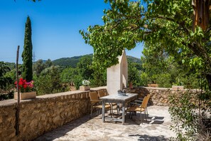 An outdoor patio with a table and chairs, surrounded by stone walls and greenery.