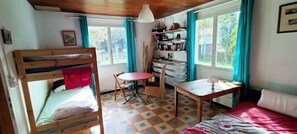 Une pièce avec des lits superposés, une table ronde, une chaise, un canapé, un bureau et une fenêtre avec des rideaux.