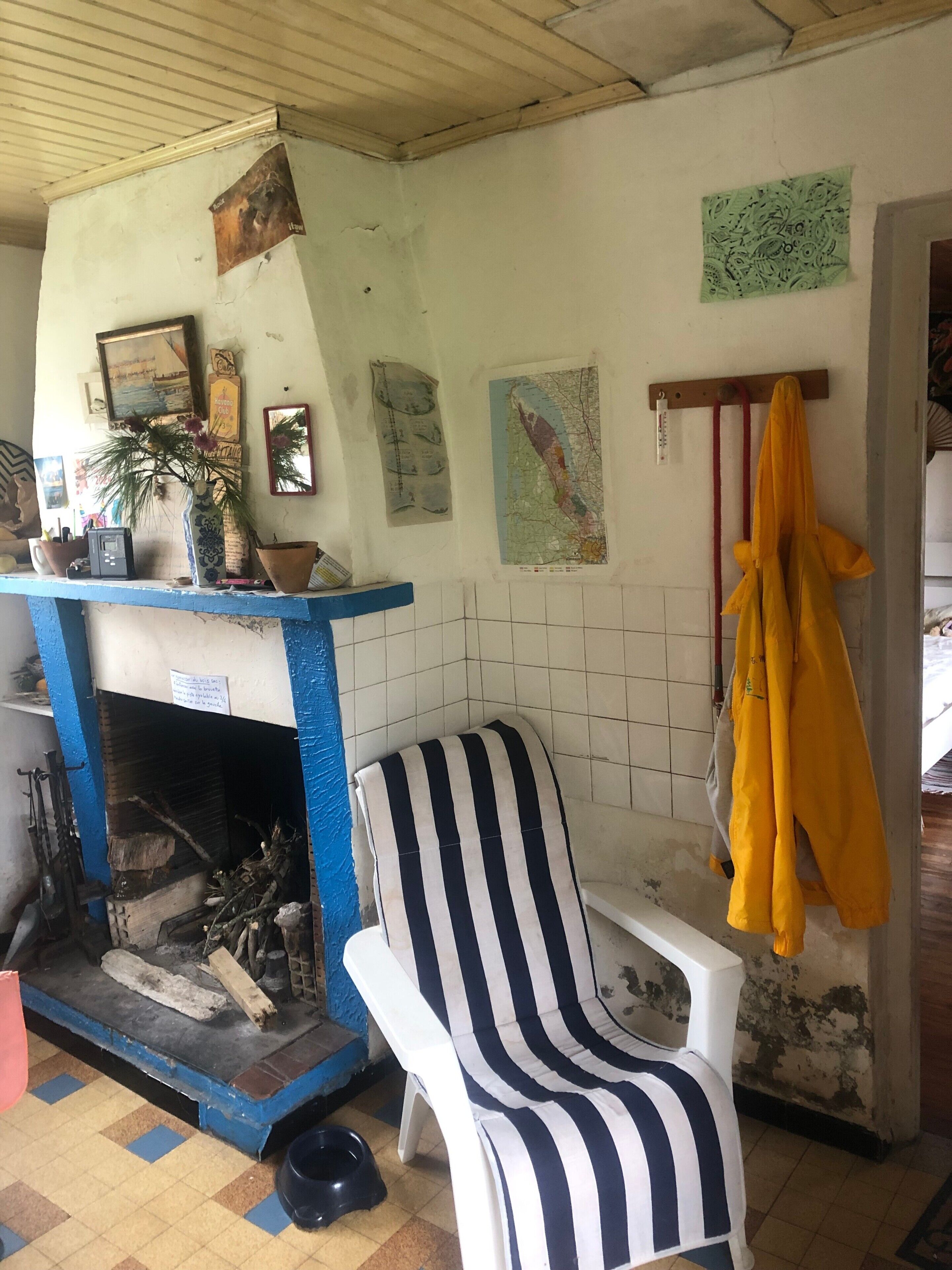 Une pièce avec une cheminée, un fauteuil à rayures, une carte accrochée au mur et une veste jaune suspendue.