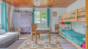 Une chambre avec un lit superposé, un lit simple, une table en bois, une chaise et une fenêtre avec des rideaux.